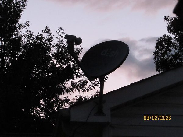 Parabole satellite fixée sur un mur, tête et câble apparents